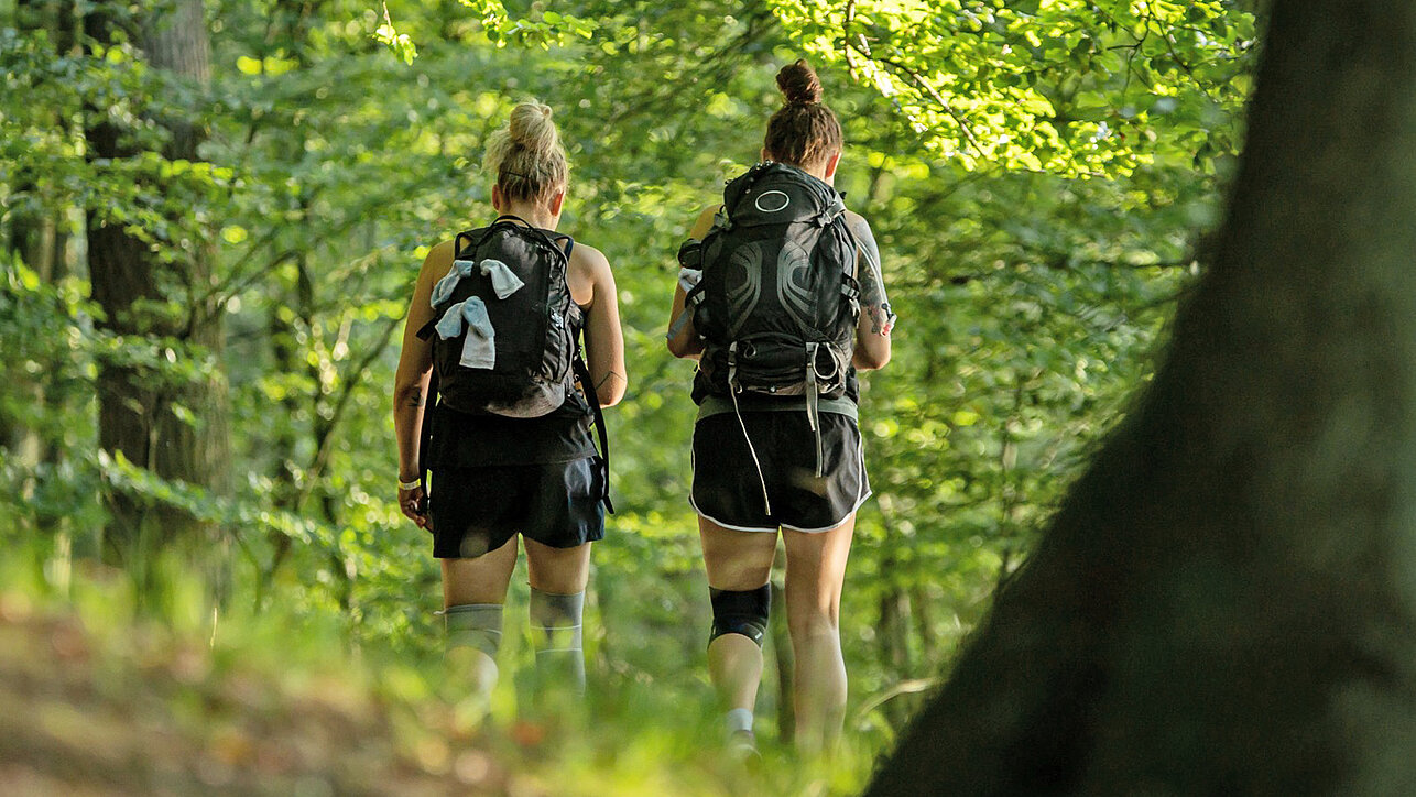 Zwei Frauen bei Wanderung mit Rucksack auf einem Waldweg ©SCC EVENTS